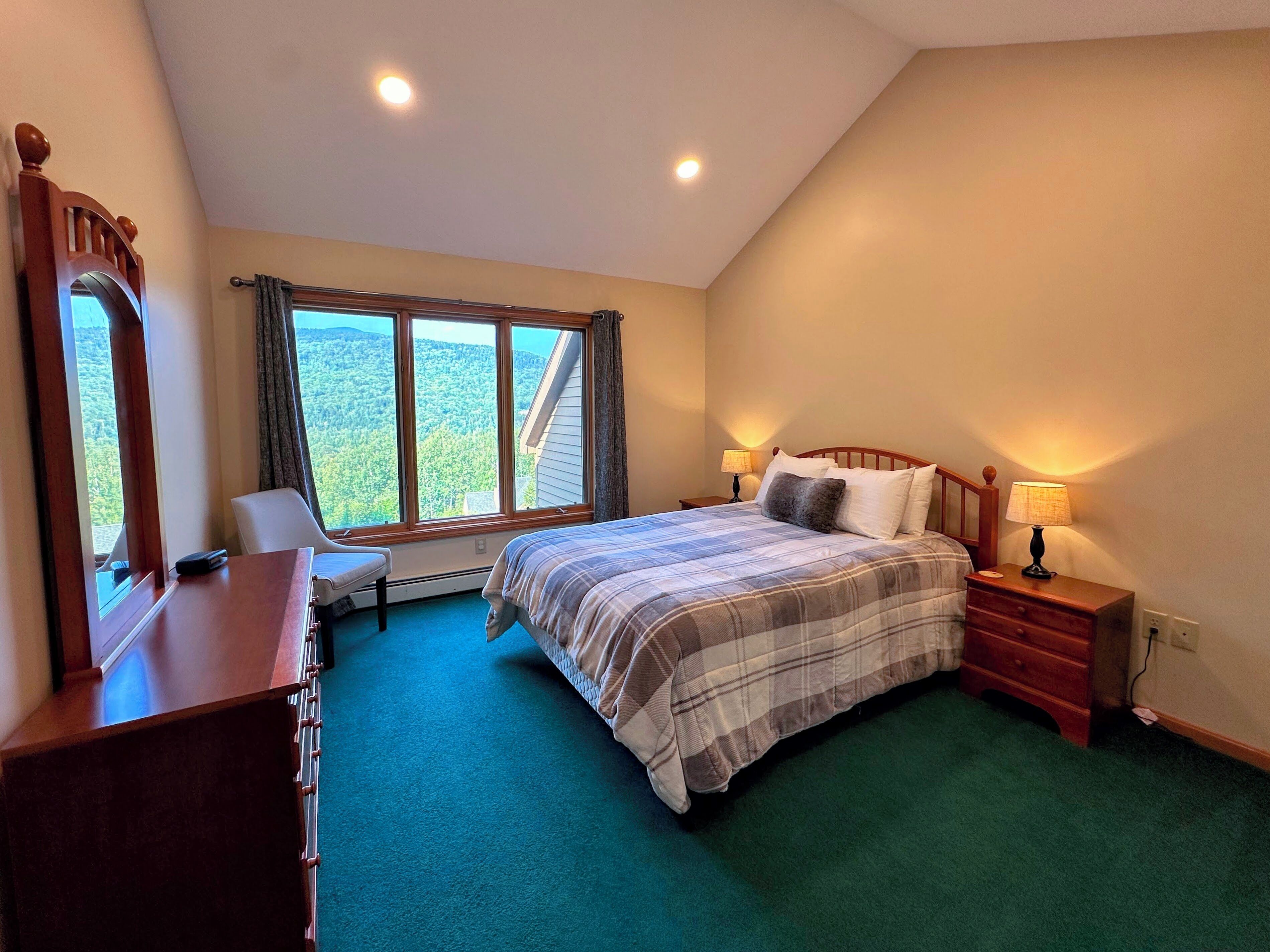 A bedroom with a large window, a bed, a desk, and a chair.