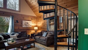 L’intérieur d’un chalet accueillant, avec un escalier en colimaçon, des murs en bois, un canapé, une table basse et une lampe.