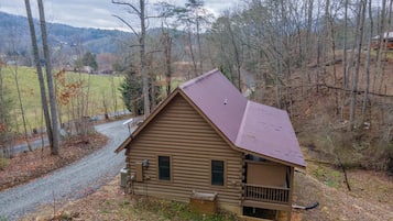 A log cabin with a sloped roof, a porch, and a gravel driveway.