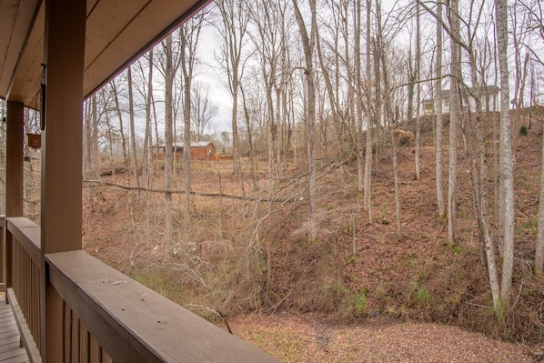 A wooden deck with a view of a forested area and a distant building. - Cozy Hot Tub Cabin! (Bryson City)