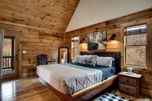 A wooden cabin bedroom with a bed, a nightstand, a chair, and a window.