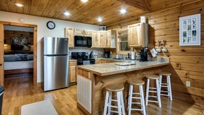 L’intérieur d’une cabane en bois comprend une cuisine équipée d’un réfrigérateur, d’un four à micro-ondes et d’une cuisinière, tous en acier inoxydable. On y trouve également des armoires en bois, un plafond en bois et un coin bar avec des tabourets.