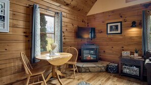 L'intérieur d'un chalet en bois comprend une table à manger, des chaises, une cheminée, un téléviseur et un tableau encadré accroché au mur.