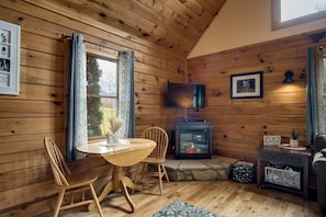A wooden cabin interior with a dining table, chairs, a fireplace, a television, and a framed picture on the wall. - Cozy Hot Tub Cabin! (Bryson City)