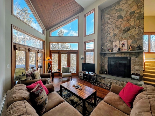 A spacious living room with a stone fireplace, large windows, and a cozy seating area. - CR6 C6 Renovated Townhome a Short Walk From the Slopes Pool gym Passes (Bretton Woods)