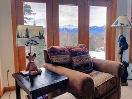 Una habitación acogedora con un sillón marrón, una mesita con un osito de peluche y una lámpara con motivos de oso.