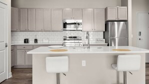 A modern kitchen with white cabinetry, stainless steel appliances, and a central island with bar stools. - Spacious Whitestown Getaway (Whitestown)