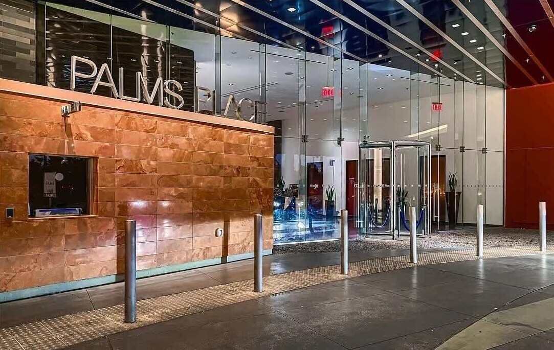 Una entrada de hotel moderna con un llamativo letrero 'PALMS', fachada de vidrio y pared roja.