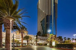 Un hotel de gran altura con un llamativo letrero 'PALMS', palmeras y una zona de entrada bien iluminada.