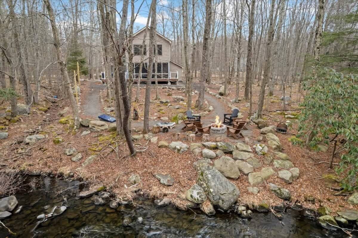 Una cabaña rodeada de bosque, con un arroyo pequeño y zona de estar al aire libre.