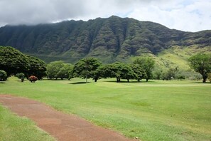 A golf course with a path leading to the tee area, surrounded by lush greenery and a mountain in the background. - @ Marbella Lane - Mesmerizing Ocean + MT Views (Waianae)
