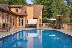 Ein Poolbereich mit Holzterrasse, Liegestühlen und Sonnenschirmen.