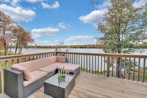 A deck with a wicker sofa and a glass table, overlooking a lake with trees and a clear sky. - Lakefront, Hot Tub, Kayaks, Firepit, Pool Table (Tobyhanna)