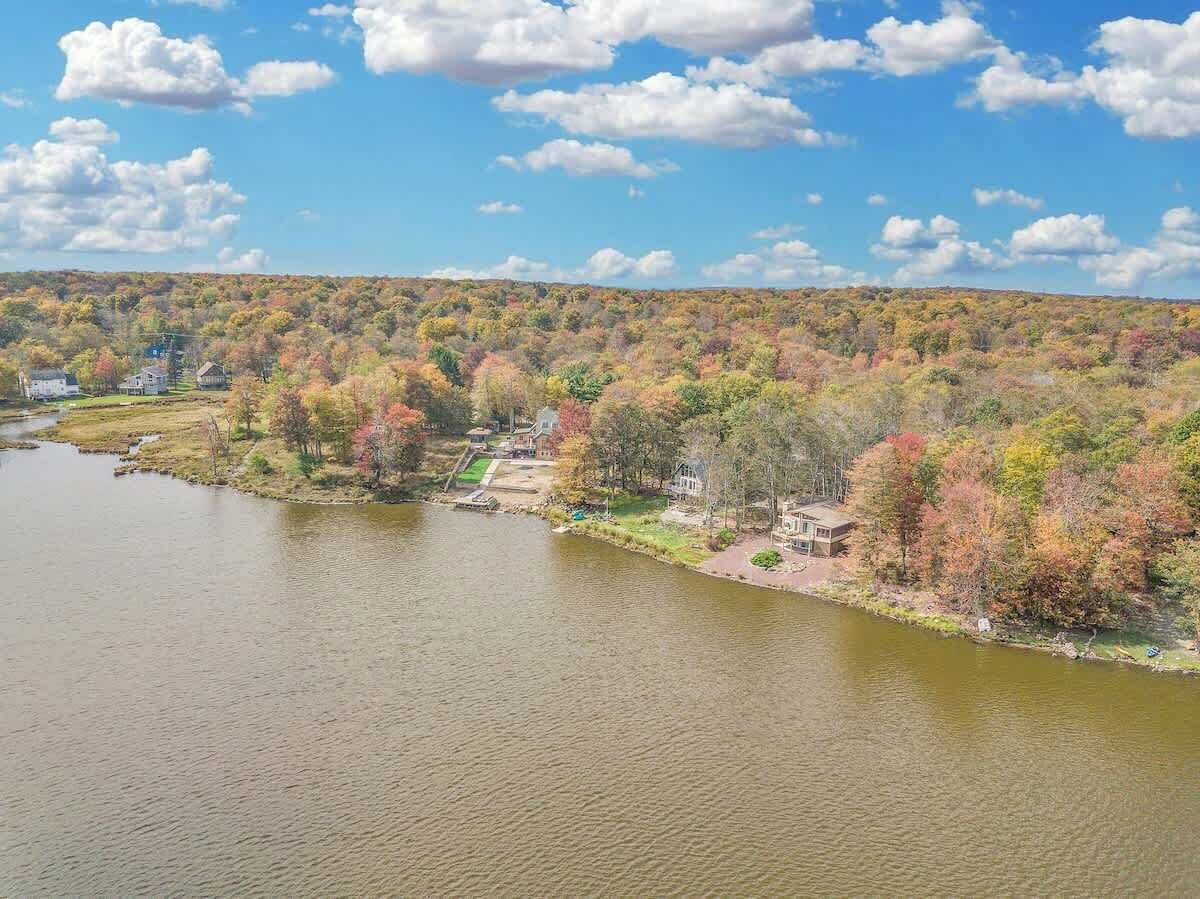 A river with houses along the banks, surrounded by trees with autumn foliage.