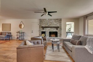 Ein Wohnzimmer mit Kamin aus Stein, Ledersofas, Deckenventilator und Blick ins Freie.