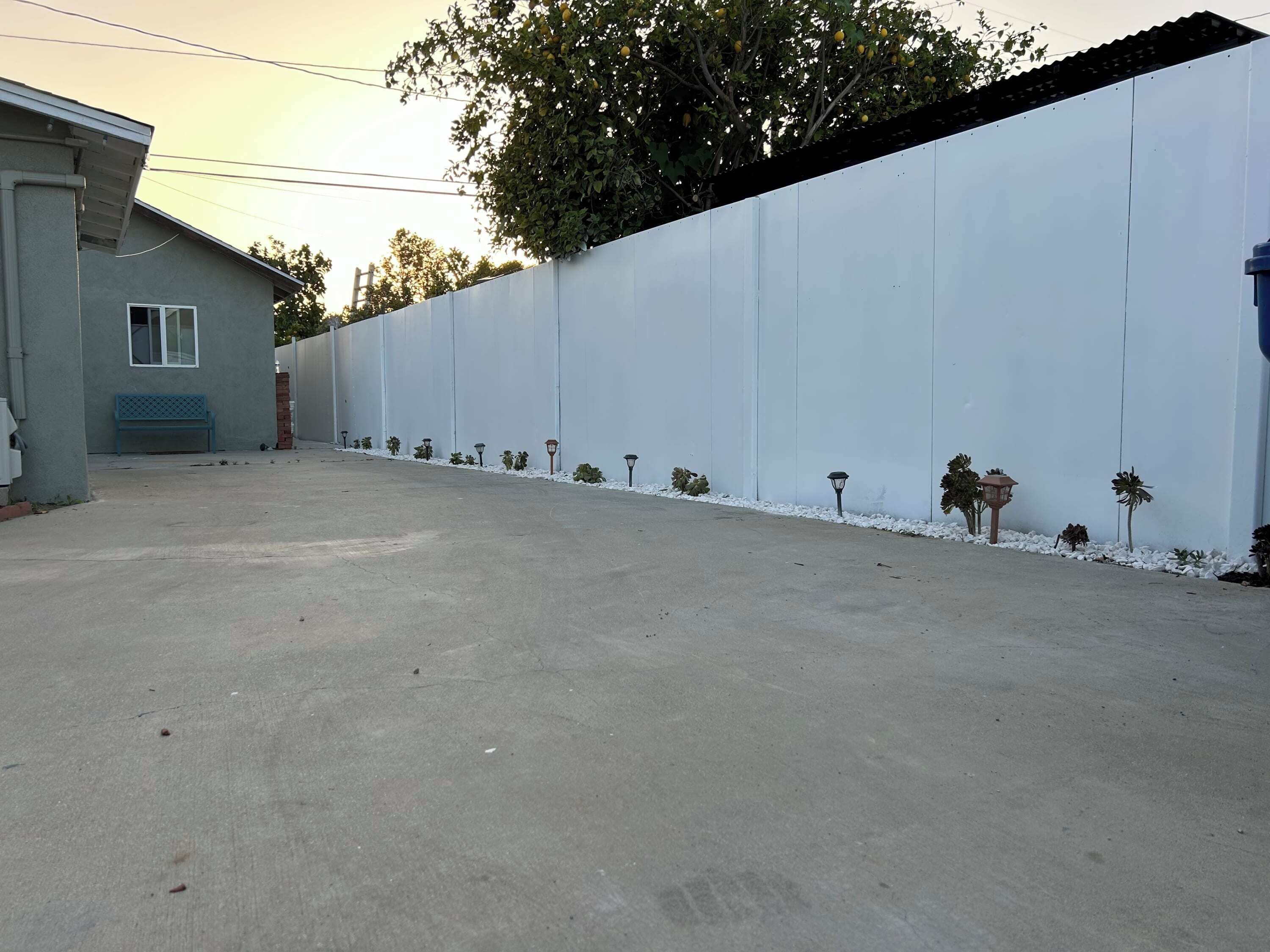 A paved parking area with a white wall, a bench, and small plants along the wall.