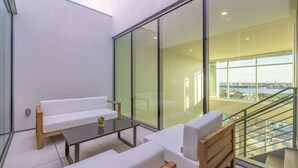 Uma varanda moderna com mobiliário branco, grandes portas de vidro e vista para a cidade.