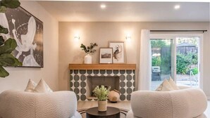Un salon moderne avec deux fauteuils confortables, une cheminée au motif géométrique et une grande fenêtre donnant sur un paysage verdoyant.