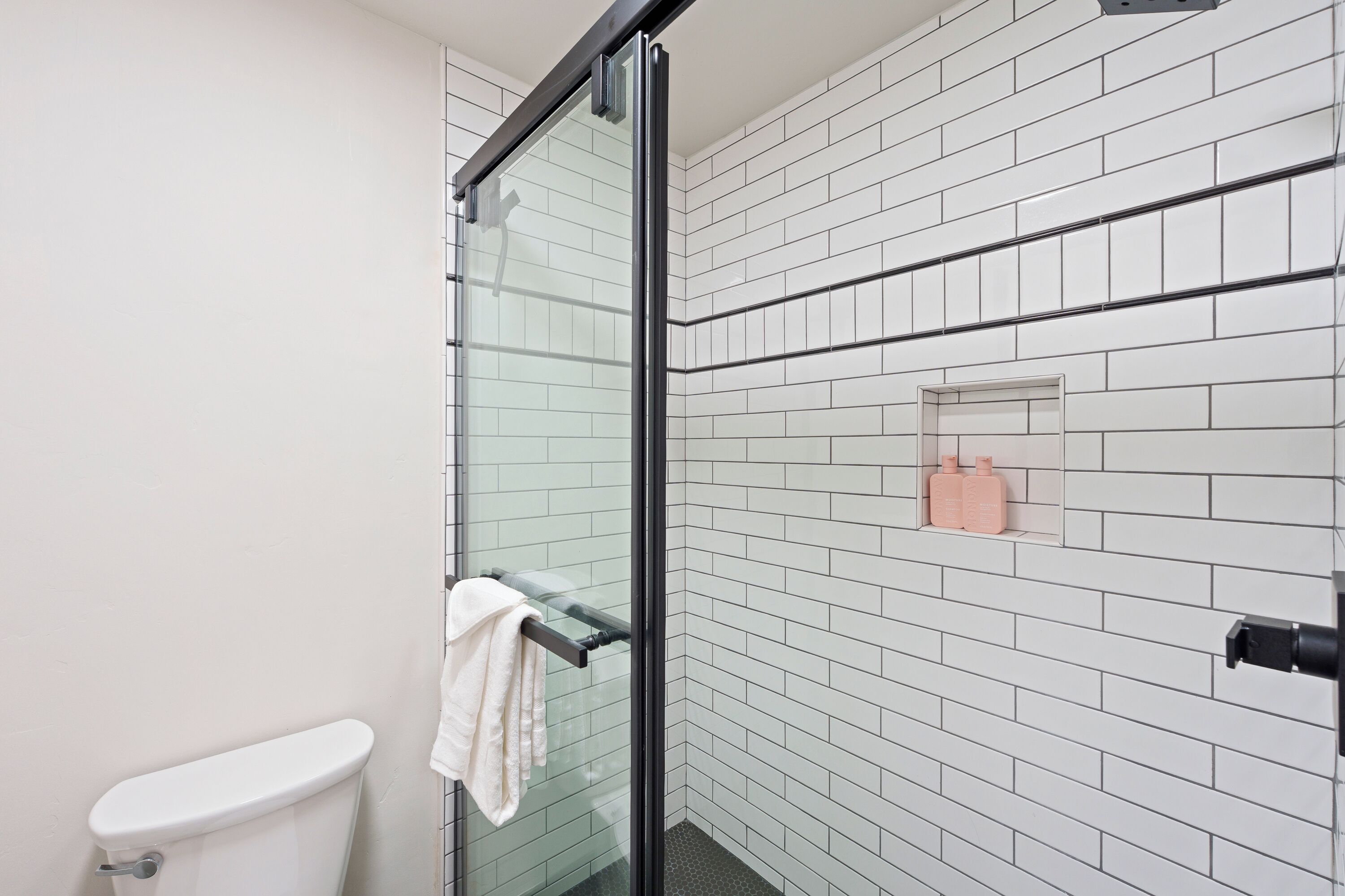 A bathroom with a glass shower enclosure, white tiled walls, and a white toilet.