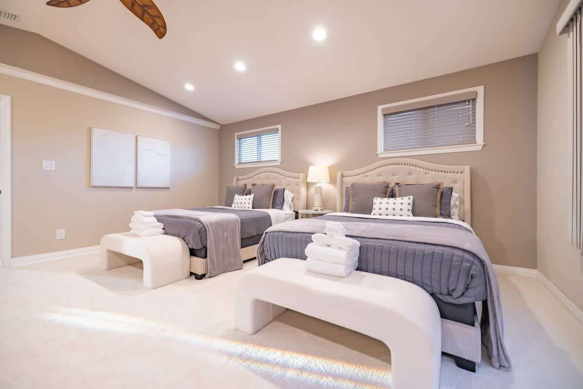 A bedroom with two beds, a bench, and a ceiling fan.