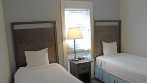 Two single beds with wooden headboards, a bedside table with a lamp, and a window with blinds.