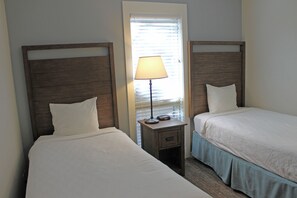 Two single beds with wooden headboards, a bedside table with a lamp, and a window with blinds. - 7th Mtn 823f (Bend)