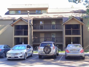 A multi-story building with a parking lot. There are three cars parked in front, including a silver SUV with a spare tire mounted on the back.