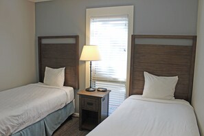 A hotel room with two single beds, a nightstand with a lamp, and a window with blinds.