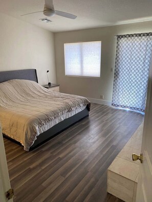 A bedroom with a bed, a ceiling fan, a window with blinds, and a patterned curtain. - @ Marbella Lane - Majestic Desert Mountain Views (Desert Hot Springs)