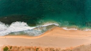 Eine Vogelperspektive eines Strandes mit sandigem Ufer und brechenden Wellen.