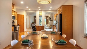 A modern kitchen with wooden cabinets, stainless steel appliances, and a dining area with a long wooden table set for four. - Slope View (Parkdale)