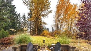 A garden with two Adirondack chairs, a lantern, and a variety of trees and plants. - Slope View (Parkdale)