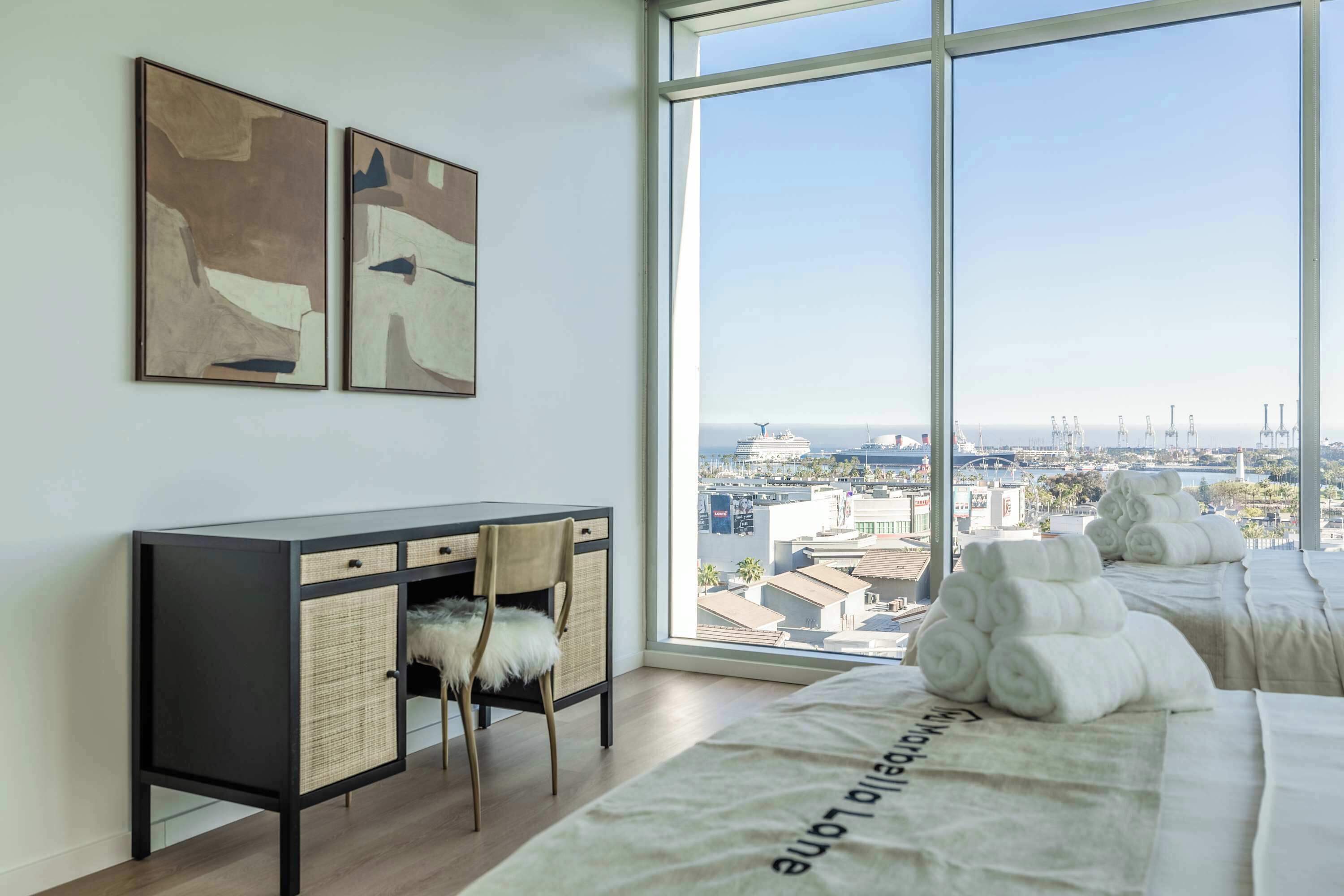 Una habitación de hotel moderna con un ventanal grande, un escritorio con cestas de mimbre y una cama con toallas.