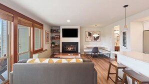 A modern living room with a fireplace, a sofa, a dining table, and a kitchen area. - Seventh Mountain 1417 (Bend)