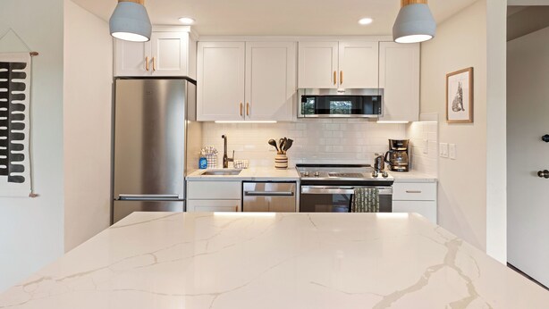 A modern kitchen with white cabinets, stainless steel appliances, and a marble island. - Seventh Mountain 1417 (Bend)