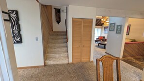 A hallway with a carpeted floor, a wooden door, and a wicker chair. - Meadow House 42 (Bend)