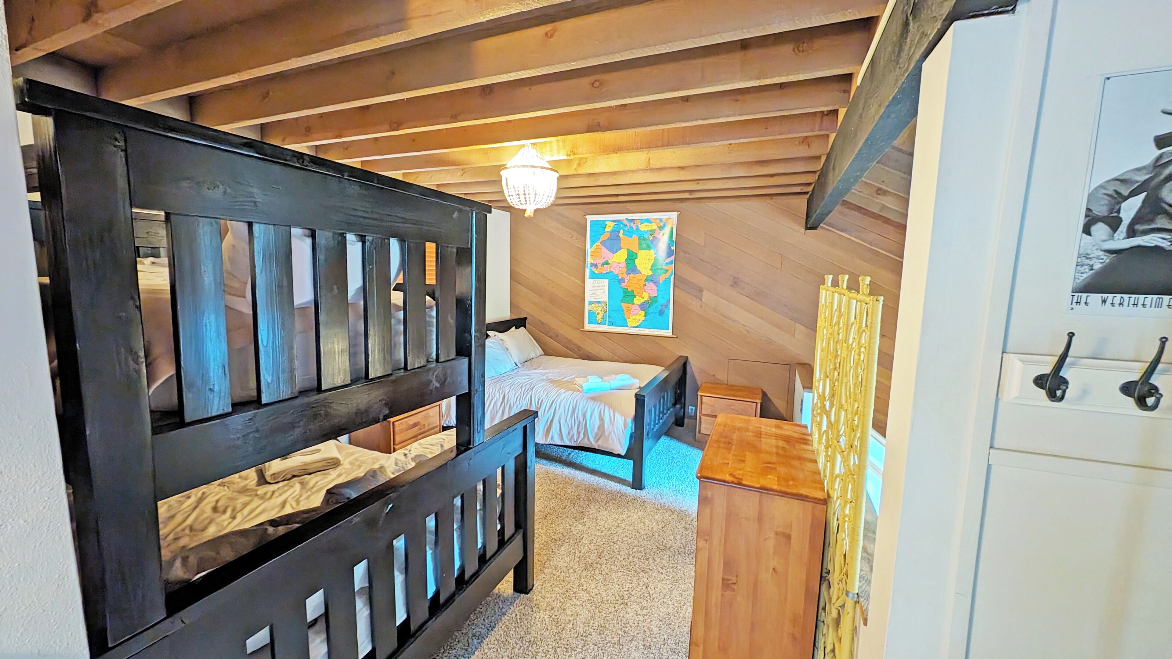 A bedroom with a bed, a wooden headboard, a map on the wall, and a chandelier.