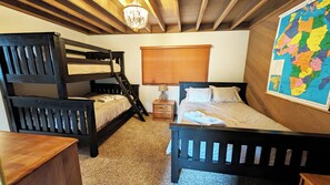 A room with bunk beds, a wooden desk, a nightstand, a lamp, and a world map on the wall.