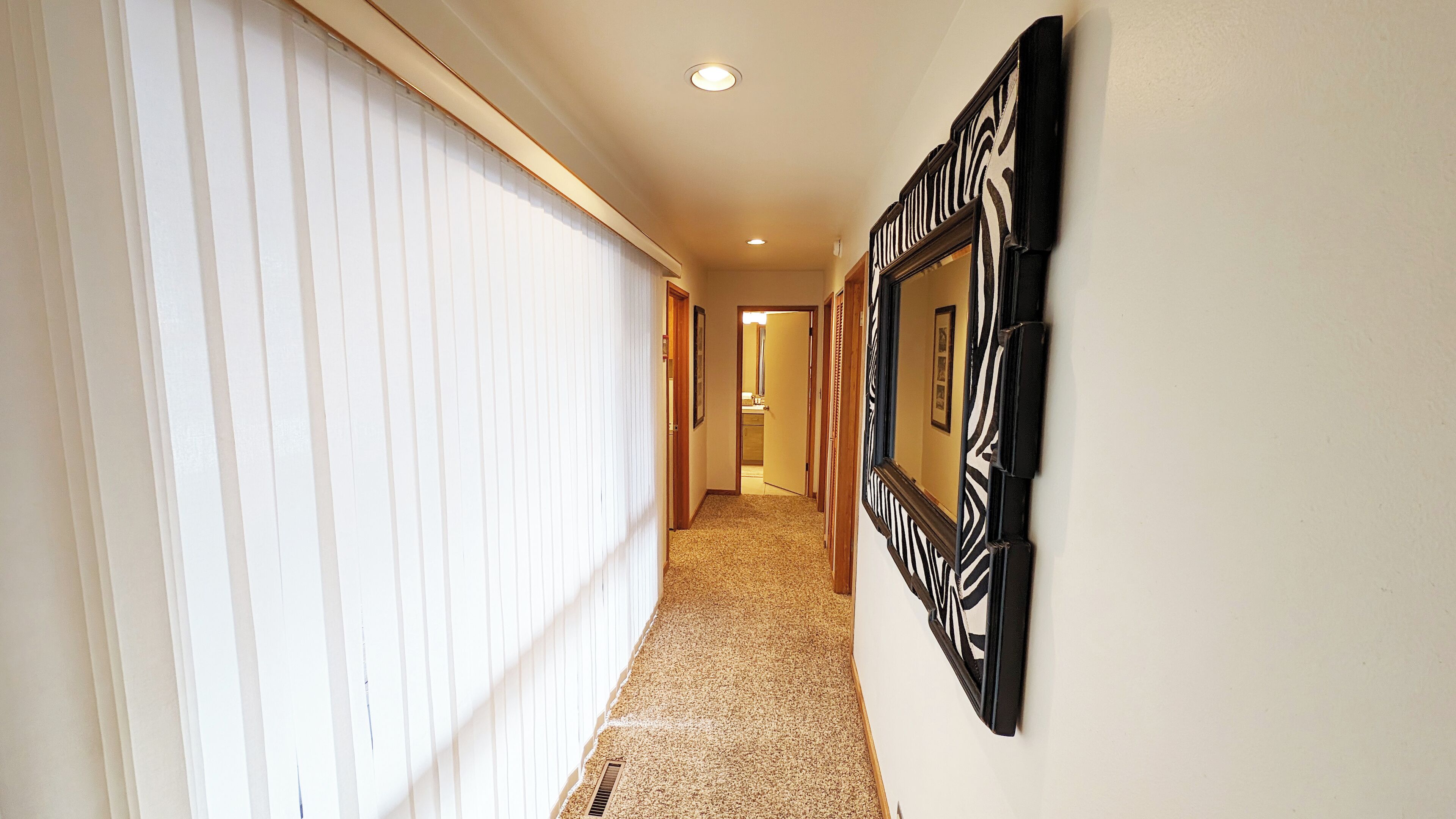 A hallway with a carpeted floor, white walls, and a black and white patterned mirror on the right.