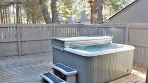Ein Whirlpool auf einer Holzterrasse mit Treppen, umgeben von einem Holzzaun und Bäumen.