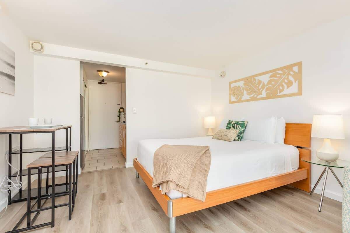 A bedroom with a bed, bedside table, lamp, and a view of the hallway.