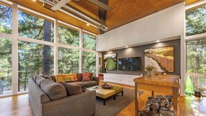 A modern living room with a large sofa, a coffee table, a TV, and a kitchen island with pots and pans. - Happenstance Vineyards King Rooms (Mosier)