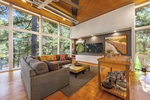 A modern living room with a large sofa, a coffee table, a TV, and a kitchen island with pots and pans.