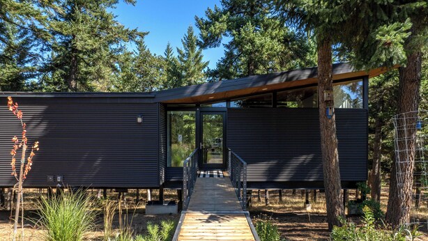 A modern building with a wooden deck leading to a covered entrance, surrounded by trees. - Happenstance Vineyards King Rooms (Mosier)