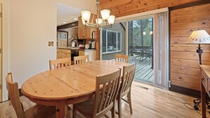 A wooden dining table with chairs, a chandelier, and a view of an outdoor deck. - Pole House 10 (Bend)
