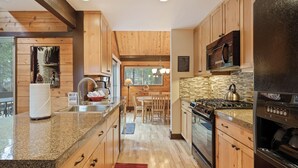 A modern kitchen with wooden cabinets, granite countertops, a stainless steel sink, a built-in microwave, and a gas stove. - Pole House 10 (Bend)