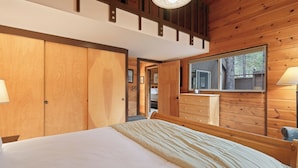 A bedroom with a large bed, wooden walls, a window, and a mirror. - Pole House 10 (Bend)