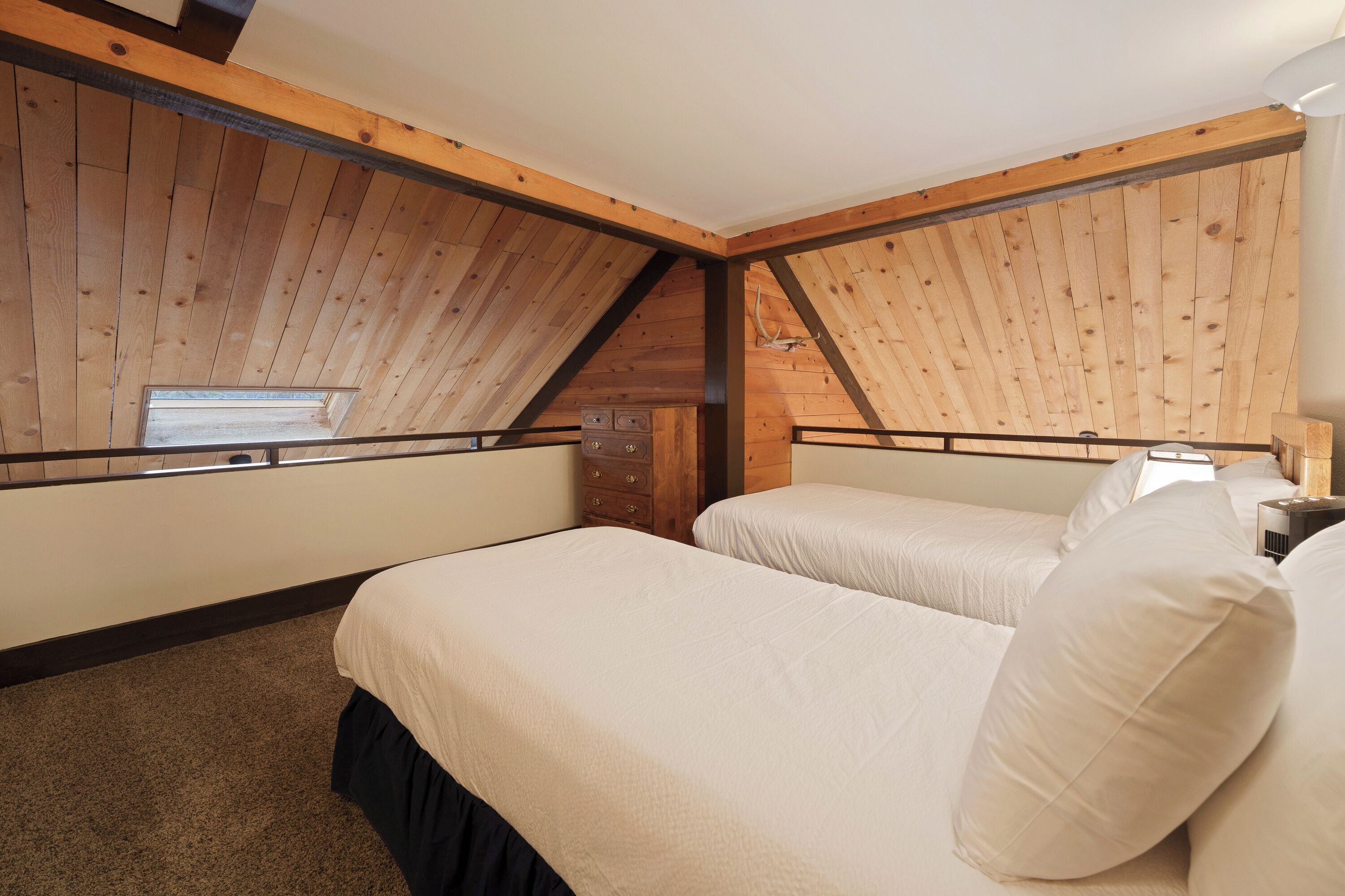 Une chambre avec deux lits, des poutres apparentes en bois au plafond, une fenêtre et une commode.
