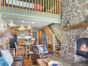 A spacious living area with a stone fireplace, a dining table, and a kitchen in the background. - Meadows Retreat 226 (Bend)