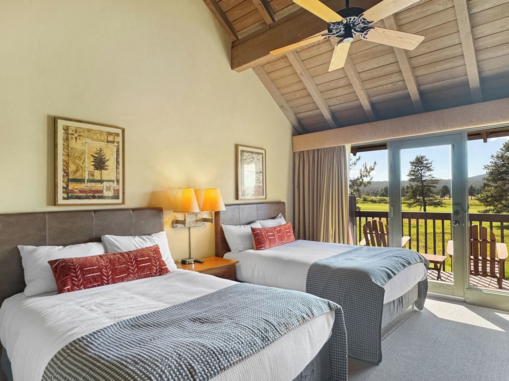 Une chambre d’hôtel avec deux lits, un ventilateur de plafond, un balcon donnant sur l’extérieur et deux lampes fixées au mur.